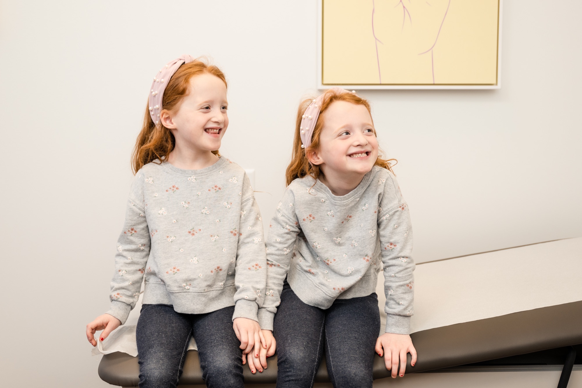 Twin sisters laughing together on the exam table during a visit to Care+ Pediatrics