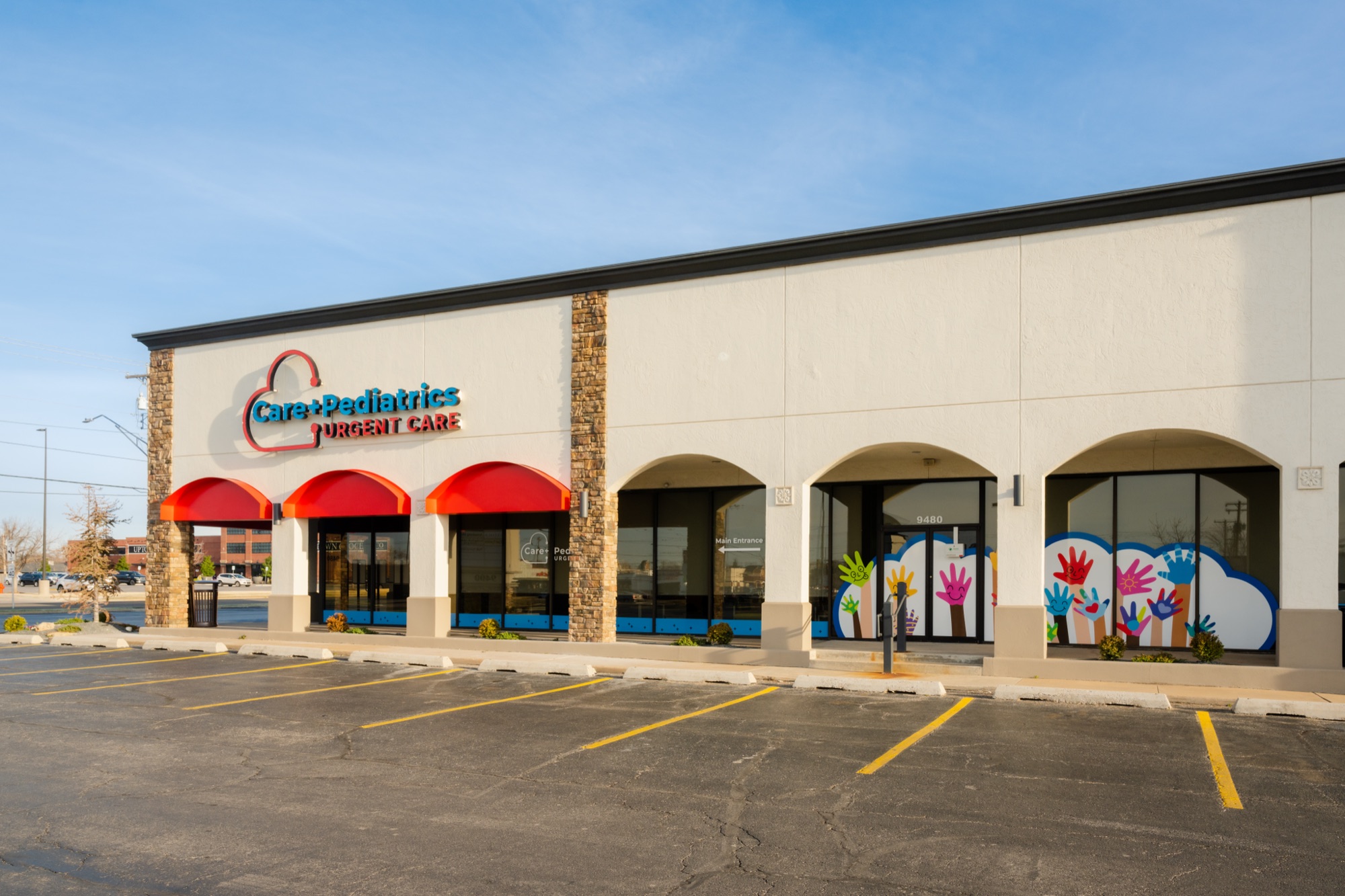 The Care+ Pediatrics Urgent Care storefront at 9480 N. May Ave with its red awnings and hand mural windows